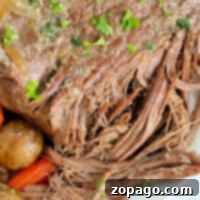 A close-up of a Ninja Foodi pot roast with carrots and potatoes, garnished with herbs.