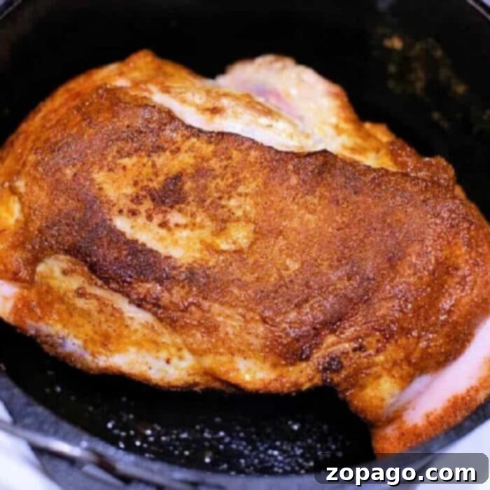 A perfectly seared and seasoned pork roast in a black cast iron Dutch oven, achieving a golden-brown crust. The aroma of a delicious slow-cooked meal fills the air.
