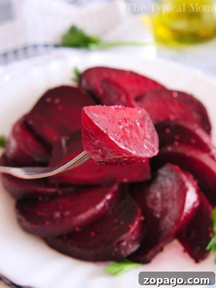 Easy Whole Instant Pot Beets 2 Close-up of a fork holding a slice of cooked beet, tenderly prepared using an Instant Pot, on a plate with more beet slices in the background.