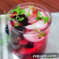 A glass of blackberry tequila thyme smash cocktail, garnished with fresh blackberries and a sprig of thyme