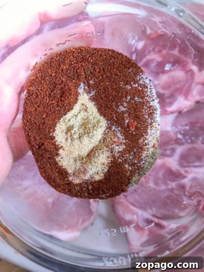 Smoky Grilled Pork Chops 2 Close-up of a raw pork chop generously coated with a savory dry rub, showcasing the spices adhering beautifully to the meat, ready for grilling.