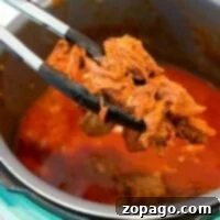Tongs carefully lift tender beef from an Instant Pot filled with rich, red sauce, embodying the essence of classic beef roast recipes.