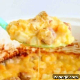 A spoon lifts cheesy hashbrown potatoes with sausage from a slow cooker.