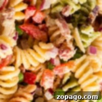 Close-up of a colorful bacon pasta salad featuring rotini, crispy bacon, red peppers, peas, and diced onions.