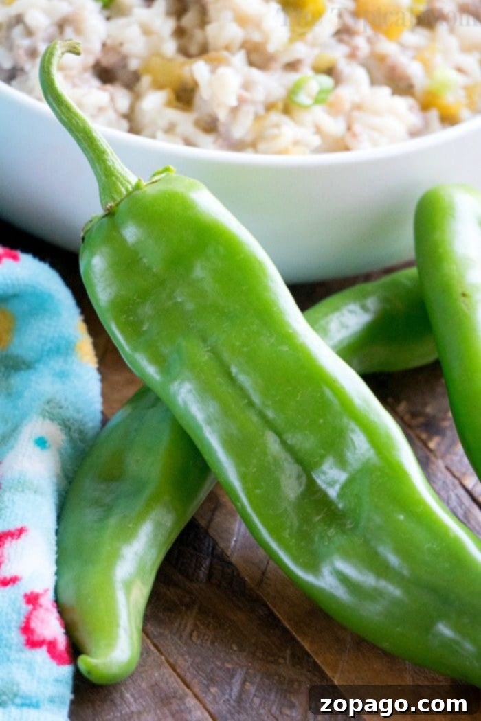 Hatch Chile Creations 3 Fresh Hatch green chili peppers rest on a wooden surface, hinting at the spicy twist in your Instant Pot sausage rice casserole, with a bowl of cooked rice in the background.