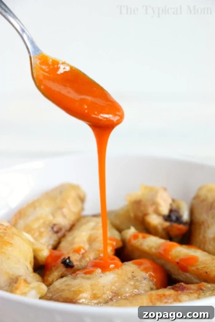 Frozen chicken wings in an air fryer actually turn out great! Tender meat on the inside with a crispy skin and smothered in sauce. It's the way to go! #frozen #wings #chickenwings #airfryer #airfryerrecipes #frozenwings Spoon drizzling bright orange sauce over a bowl of crispy chicken wings straight from the air fryer.