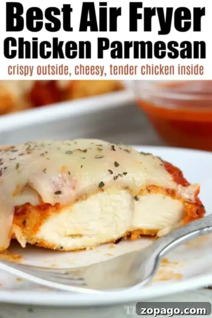 Best Air Fryer Chicken Parmesan: Crispy Outside, Cheesy, Tender Chicken Inside Close-up of a slice of air fryer chicken parm on a white plate, topped with melted cheese and fresh herbs. The background shows a blurred dish and a small bowl of sauce.