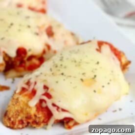 Air fryer chicken parm topped with melted cheese and herbs on a white plate.