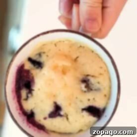Blueberry Mug Bliss 5 A close-up of a hand holding a mug with a baked blueberry muffin, showcasing its fluffy texture and visible blueberries.