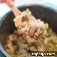 Velvety Instant Pot Mushroom Rice 5 A hand gracefully serves a delightful instant pot cream of mushroom rice dish from a pot with a wooden spoon.