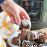 A hand holds an iced air fryer donut made with cinnamon rolls, with the trusty ninja foodi in the background.