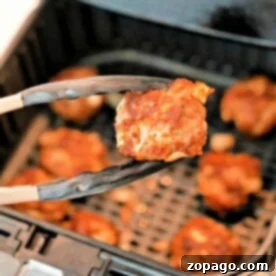 Close-up of tongs holding a piece of cooked homemade meatballs in front of an air fryer perfectly browned and crispy
