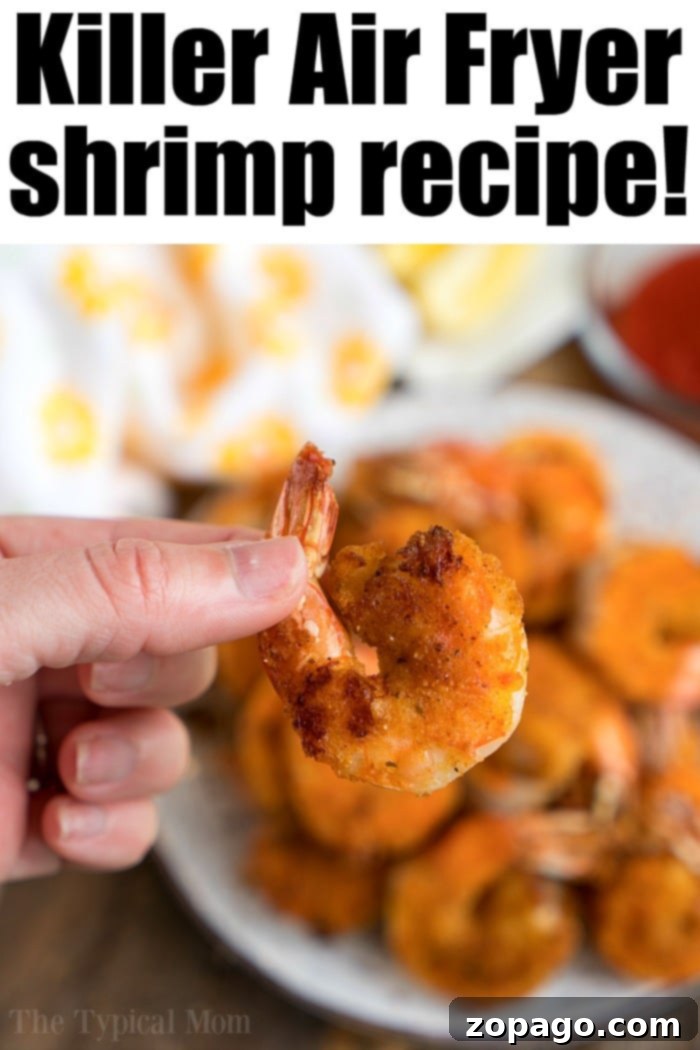 Air fryer shrimp is amazing! With a light breading & tons of flavor they're crispy to perfection in just a few minutes with NO frying required. A hand holding a piece of crispy air fryer fried shrimp, with more shrimp on a plate in the background.