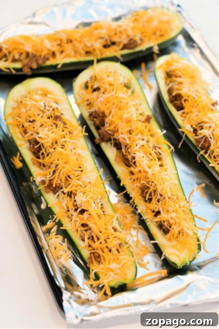 Taco-Filled Zucchini Boats 2 Roasted zucchini taco boats filled with seasoned meat and cheese, fresh out of the oven, on a baking sheet.