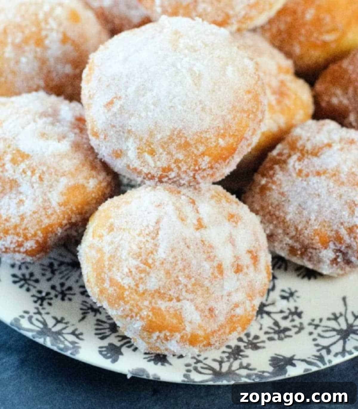 Homemade Donut Bites 5 A top-down view of freshly prepared homemade powdered sugar donut holes on a white plate, ready to be enjoyed.