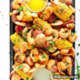 A tray of instant pot shrimp boil with corn, potatoes, sausage, herbs, and two bowls of dipping sauces.