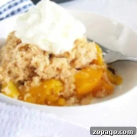 A bowl of instant pot peach cobbler crowned with whipped cream, with a fork waiting eagerly by the side.