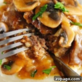 Close-up of Instant Pot Salisbury steak with mushroom gravy and mashed potatoes, garnished with parsley, being cut with a fork.