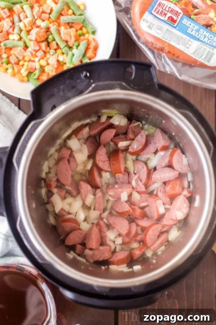 Instant Pot sausage and rice is so good! A cheesy casserole packed with smoked sausage, tender rice and vegetables cooked all in one pot in no time at all. #instantpot #instantpotrecipes #sausage #rice #casserole #cheesy #pressurecooker #ninjafoodi A vibrant close-up of pressure cooker sausage and rice casserole, rich with melted cheese and fresh herbs.