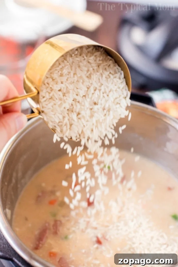 One-Pot Wonder Cheesy Sausage and Rice 5 Pouring uncooked rice from a measuring cup into the Instant Pot of simmering sausage and rice casserole