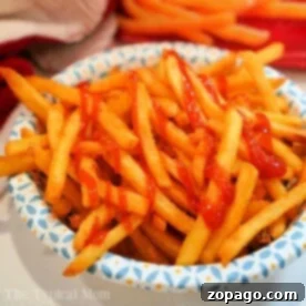 A bowl of crispy air-fried french fries drizzled with ketchup.