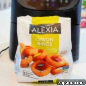 A bag of Alexia crispy frozen onion rings sits in front of an air fryer on a white countertop, ready to be cooked to perfection.