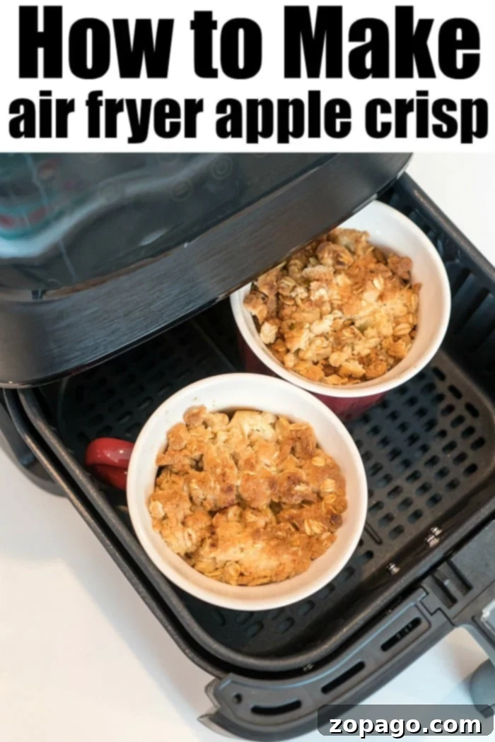 Golden Air Fryer Apple Oat Crisp 8 Two mugs of air fryer apple crisp, one in focus with a crisp golden topping, on a wooden board.