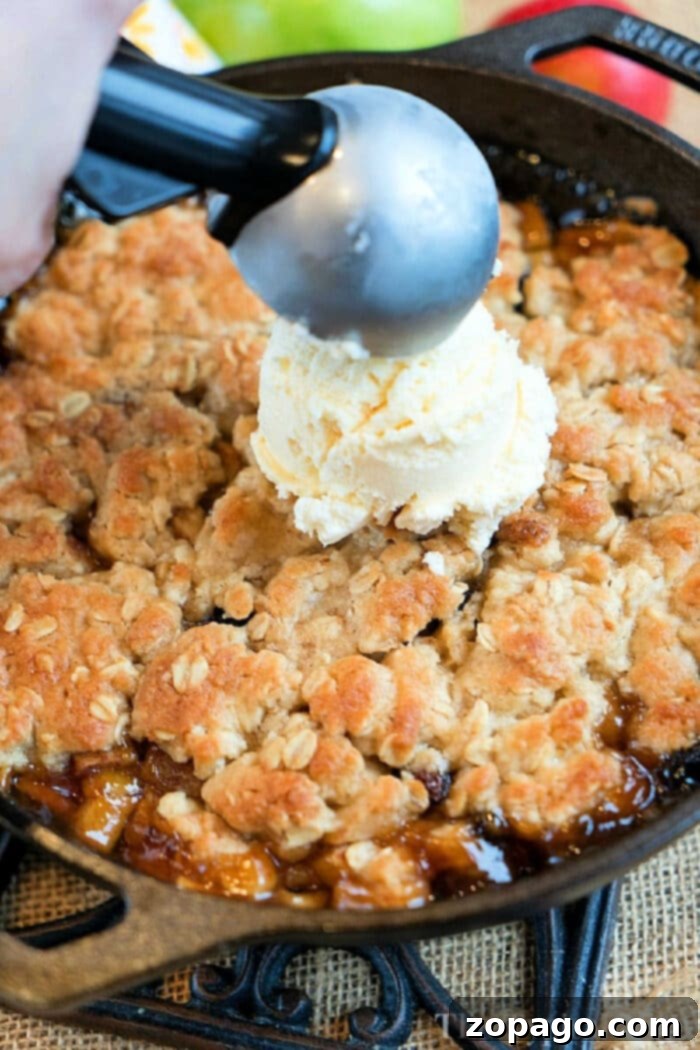 Skillet Apple Crisp with Oat Crumble 2 Scooping rich vanilla ice cream onto a warm, freshly baked cast iron apple crisp, highlighting the bubbling fruit and golden oat topping.