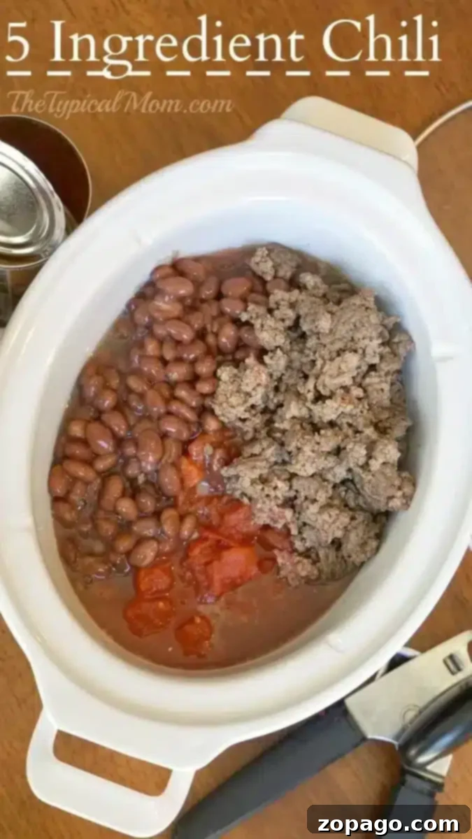 An overhead view of a white slow cooker containing 5-ingredient chili. The chili consists of beans, ground meat, and diced tomatoes.