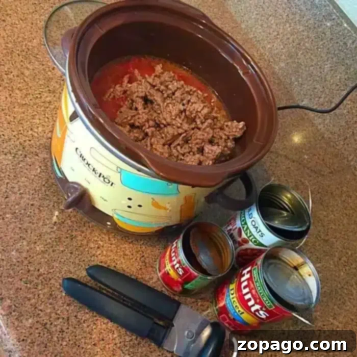 A 5 ingredient crockpot chili recipe sits on a countertop, with a slow cooker containing browned ground meat and tomato sauce.