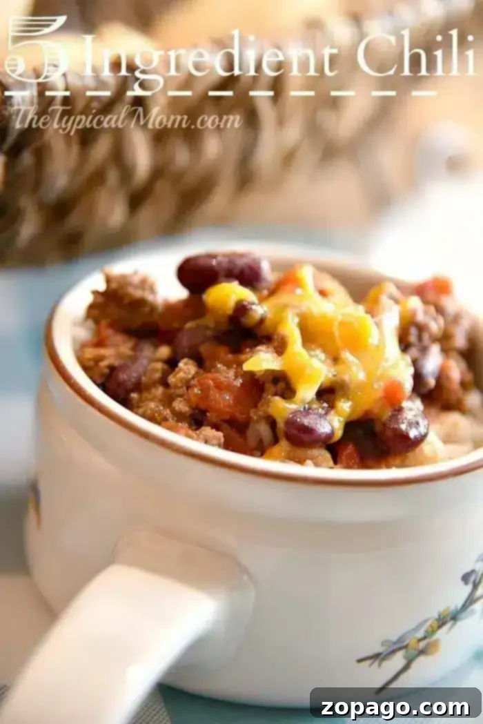 A close-up of a bowl of 5 ingredient crockpot chili recipe is shown. The chili consists of ground meat, beans, tomatoes, and is topped with shredded cheese.