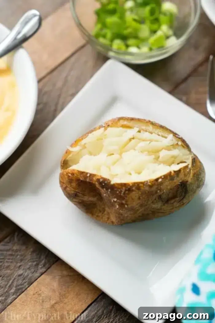 A baked potato with the top cut open, showing the fluffy interior, is placed on a white plate on a wooden table.