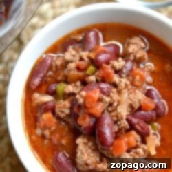 A bowl of instant pot chili with kidney beans, ground meat, and vegetables sits next to a bowl of shredded cheese.