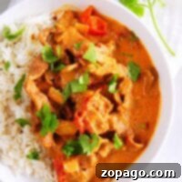 A bowl of rice topped with creamy instant pot butter beef curry, tomatoes, and cilantro.
