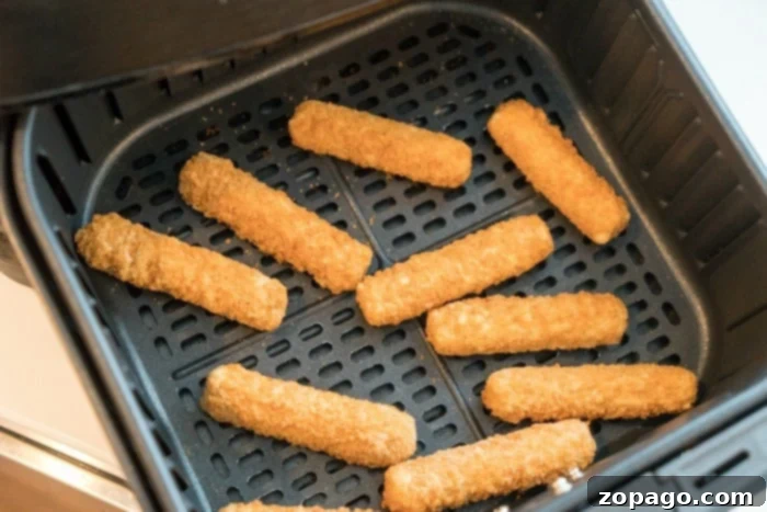 Crispy Air Fryer Mozzarella Sticks 2 A close-up of golden, crispy frozen mozzarella sticks in an air fryer basket, perfectly cooked.