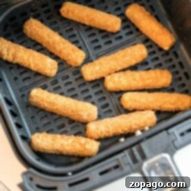 Frozen mozzarella sticks are neatly arranged in an air fryer basket, ready to be cooked.