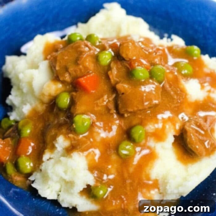 Ultimate Ninja Foodi Stew 2 Mashed potatoes topped with hearty beef stew, peas, and carrots, all perfectly cooked in a Ninja Foodi, served on a blue plate.