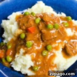 Mashed potatoes topped with hearty beef stew, peas, and carrots, all perfectly cooked in a Ninja Foodi, served on a blue plate.