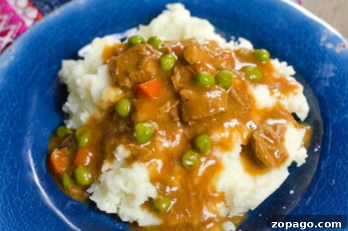 Ultimate Ninja Foodi Stew 7 Mashed potatoes topped with a savory ninja foodi stew, peas, and carrots rest elegantly on a blue plate.
