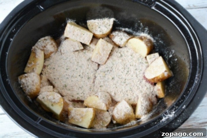 Hearty Crockpot Steak and Potatoes 4 Sliced potatoes with seasoning nestle alongside tender crockpot steak in a black slow cooker.