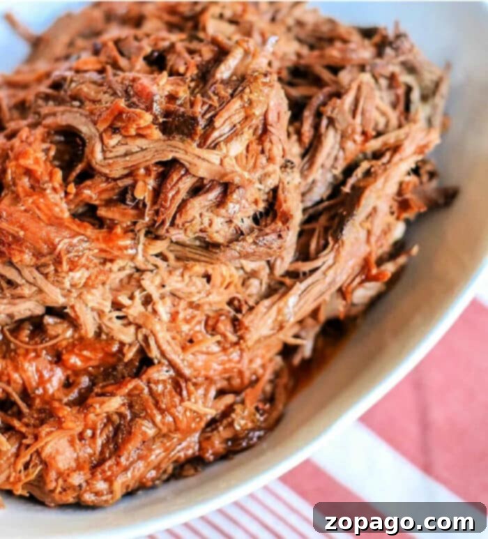 Tender Slow Cooker BBQ Beef 2 Crockpot BBQ Beef, tender and flavorful, sits shredded in a white dish on a table with a red and white striped cloth.
