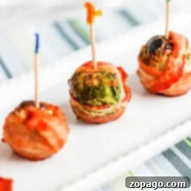Three crispy Brussels sprouts with bacon, held together by toothpicks, stand in a row on a white rectangular plate, arranged on a striped surface.