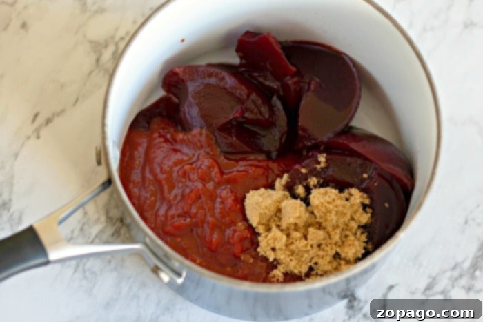 Ingredients for the Cranberry Meatball Sauce A saucepan with sliced cranberry sauce, ketchup, and brown sugar sits on a marble countertop, ready to enhance your cranberry meatballs with its tangy sweetness.