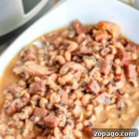 A bowl of black-eyed peas with chunks of meat in a savory broth, perfectly crafted from a tried-and-true crockpot black-eyed peas recipe, sits invitingly beside the slow cooker.