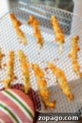 Hand holding an oven rack with crispy breaded zucchini fries, fresh from the oven—perfect for fans of Air Fryer Green Bean Fries looking to try a tasty twist.