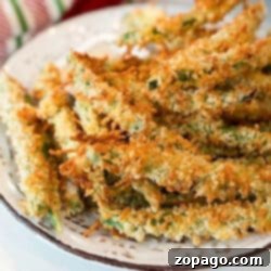 A plate of golden-brown, crispy air fryer green bean fries. They are sprinkled with crumbs and arranged in a heap on a rustic white plate, creating an appetizing display.