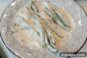 Crispy Air Fryer Green Beans 8 Air Fryer Green Bean Fries coated in flour rest on a decorative white plate, ready to be perfectly crisped by frying or baking.