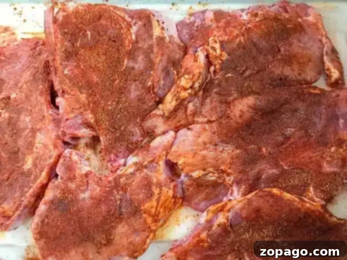 Flavorful Dry Rub Baked Pork Chops 5 Raw pork chops, richly seasoned with a reddish spice blend, are evenly spread on a white surface, preparing them for baking into the best baked pork chops.