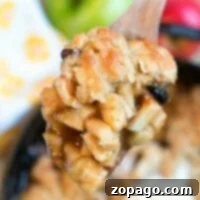 Close-up of a spoonful of apple crisp drizzled with caramel sauce; apples and vanilla ice cream temptingly await in the background.