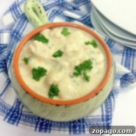 Easy Ninja Foodi Chicken Gnocchi Soup 5 A ceramic bowl filled with creamy instant pot gnocchi soup garnished with parsley sits on a blue and white checkered cloth. A stack of white plates rests in the background.